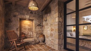 Quarto com paredes de pedra, uma cadeira de madeira, um vaso grande e uma luminária de fibra.