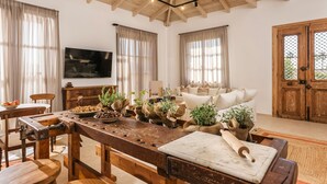 Uma cozinha rústica com vigas de madeira, uma mesa de madeira comprida e uma TV fixada na parede.