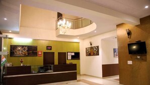 A hotel reception area with a reception desk, a chandelier, artwork on the walls, and a television mounted on the wall. - Hotel Grand Ranthambore (Sawai Madhopur)