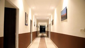 A long, well-lit hallway with a brown and white color scheme, leading to a darkened room at the end. - Hotel Grand Ranthambore (Sawai Madhopur)
