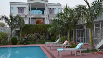 A large, two-story building with a swimming pool, palm trees, and lounge chairs.