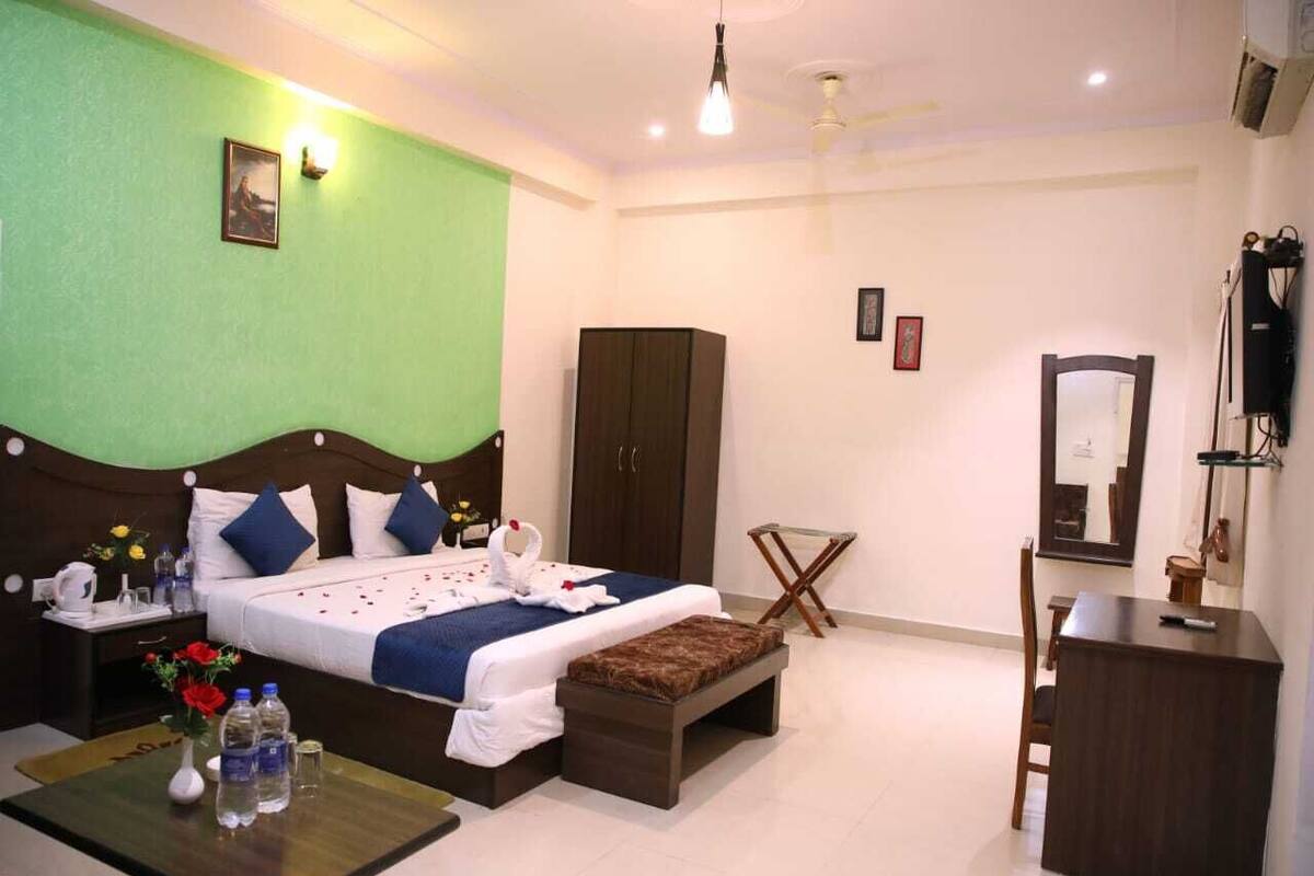 A hotel room with a bed, a wardrobe, a desk, a mirror, and a small table with water bottles.