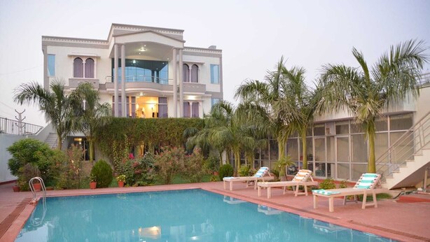 A pool area with lounge chairs and a large building with multiple windows and balconies. - Hotel Grand Ranthambore (Sawai Madhopur)