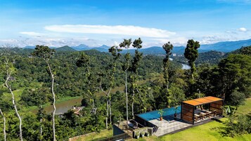 Una villa moderna con piscina, rodeada de exuberante vegetación y un río.