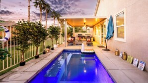 A swimming pool with a lounge area, palm trees, and a covered patio.
