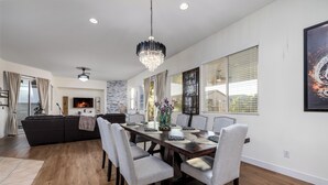 A modern dining area with a wooden table, grey upholstered chairs, and a chandelier.