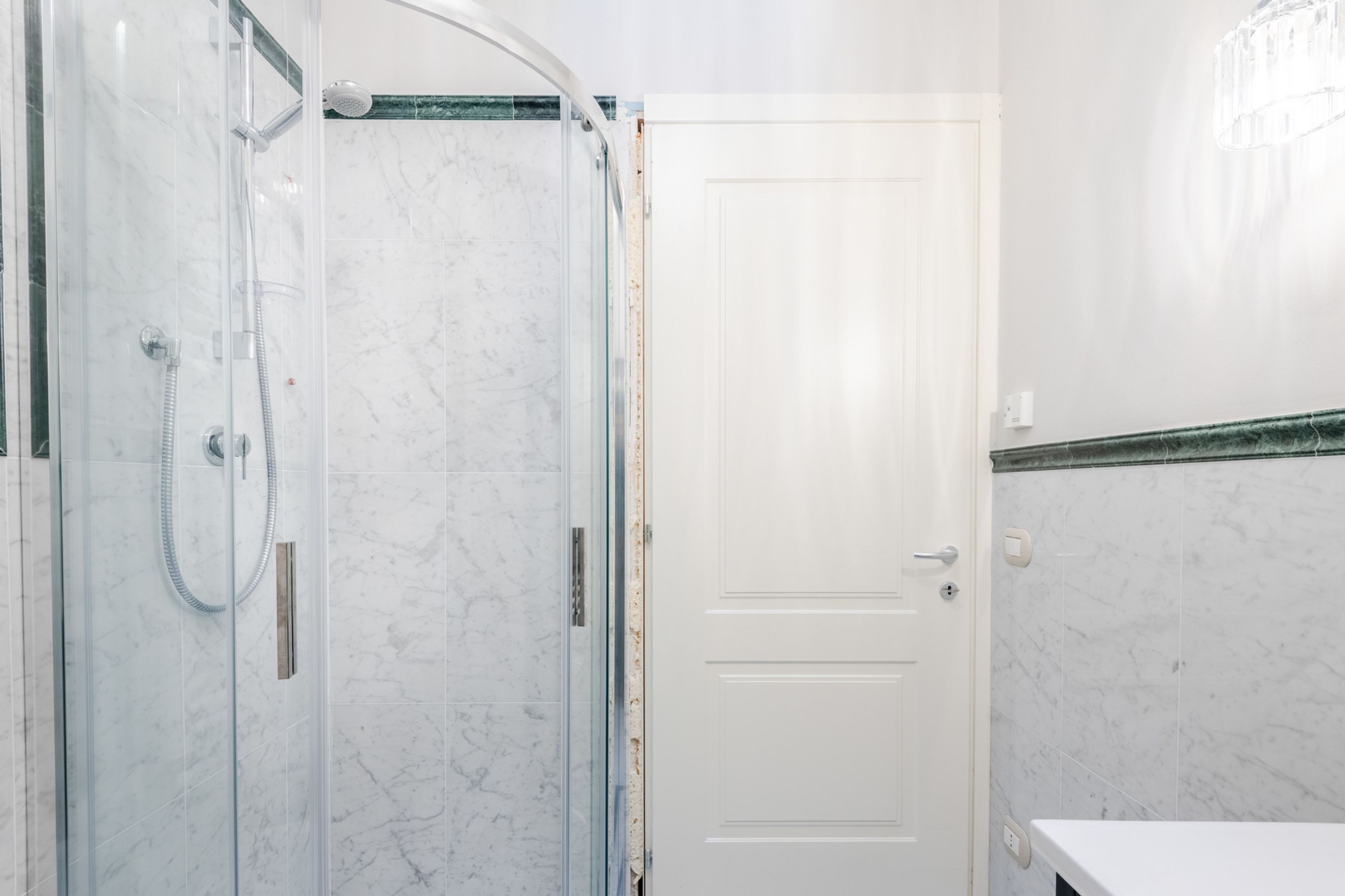 Une salle de bain avec une douche à parois de verre, une porte blanche et un mur recouvert de carreaux de marbre.