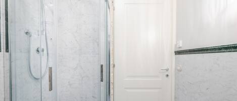 Une salle de bain avec une douche à parois de verre, une porte blanche et un mur recouvert de carreaux de marbre.