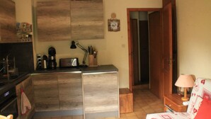 Une cuisine compacte équipée d’une cuisinière intégrée, d’une machine à café et d’un petit coin repas avec une table et une chaise.