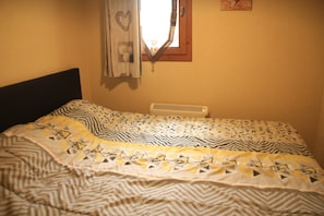 A bed with patterned bedding, a window with a heart-shaped decoration, and a wall-mounted heater. - Voinettes B5 Vnb5 Telecabine & Mountain 4 Pers (Chatel)
