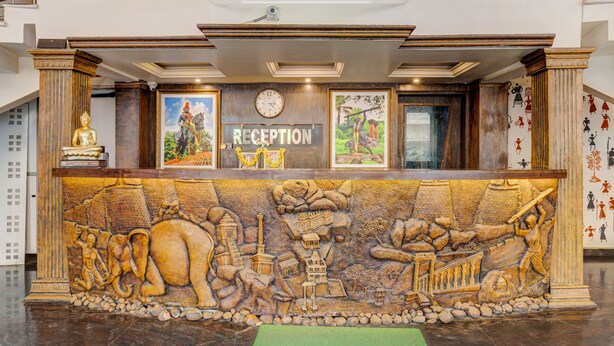 A reception desk with a mural depicting elephants and traditional buildings, a clock, and a sign that reads "RECEPTION". - IROOMZ Eco - HOTEL BIG BOSS (Chitradurga)