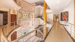 A multi-level interior with a spiral staircase, a mural with cultural motifs, and a corridor leading to a room with a large painting. - IROOMZ Eco - HOTEL BIG BOSS (Chitradurga)