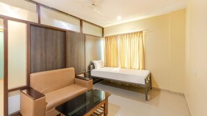 A modern room with a sofa, a bed, a glass coffee table, and a ceiling fan. - IROOMZ Eco - HOTEL BIG BOSS (Chitradurga)