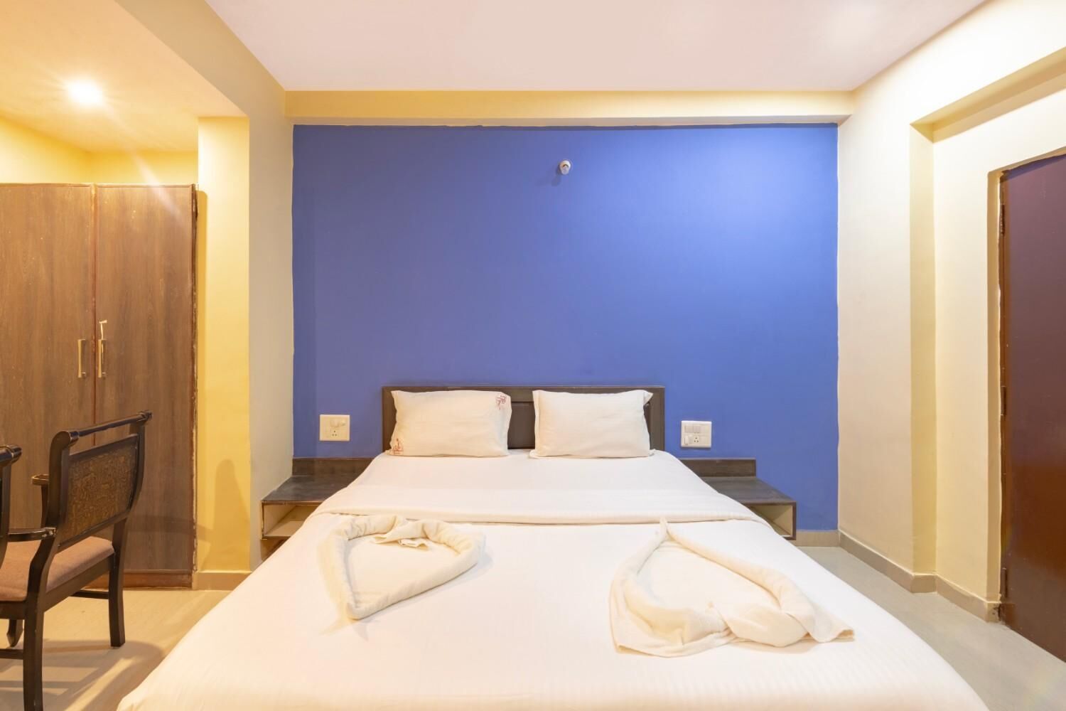 Ett hotellrum med en stor säng, två kuddar, en garderob i trä och en stol.