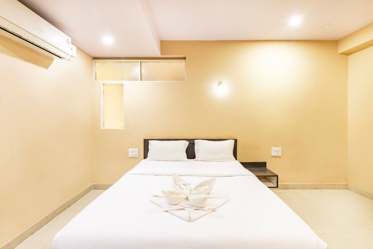 A hotel room with a bed, bedside table, and an air conditioning unit.