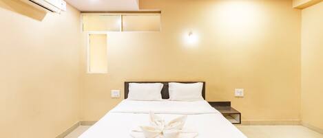 Una habitación de hotel con cama, mesita de noche y aire acondicionado.