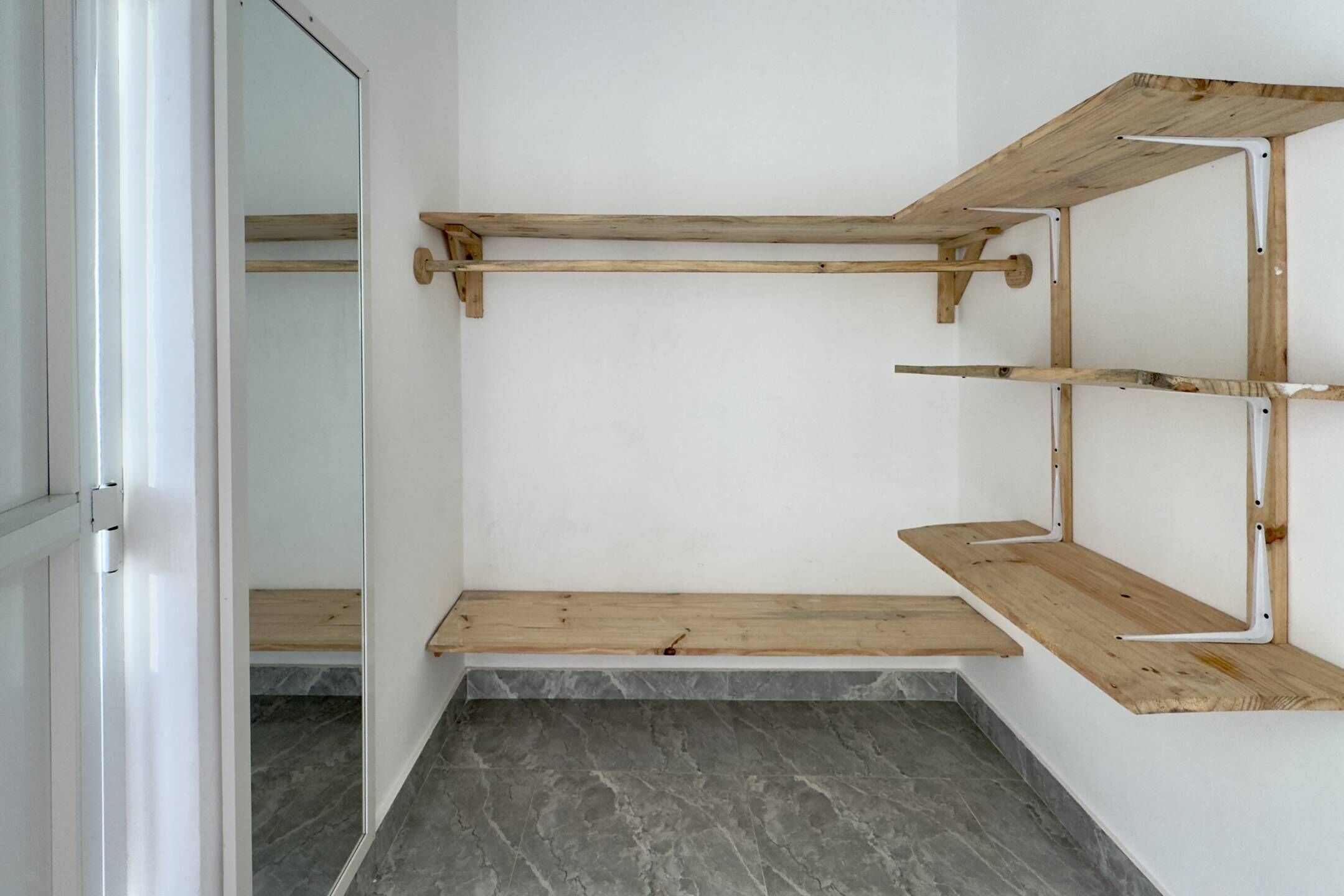 A room with a wooden shelf unit against the wall, a marble-tiled floor, and a door leading to another room.