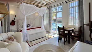 Ein Zimmer mit einem weißen Sofa, einem Bett mit Baldachin, einem Esstisch mit Stühlen und einer Gitarre an der Wand.