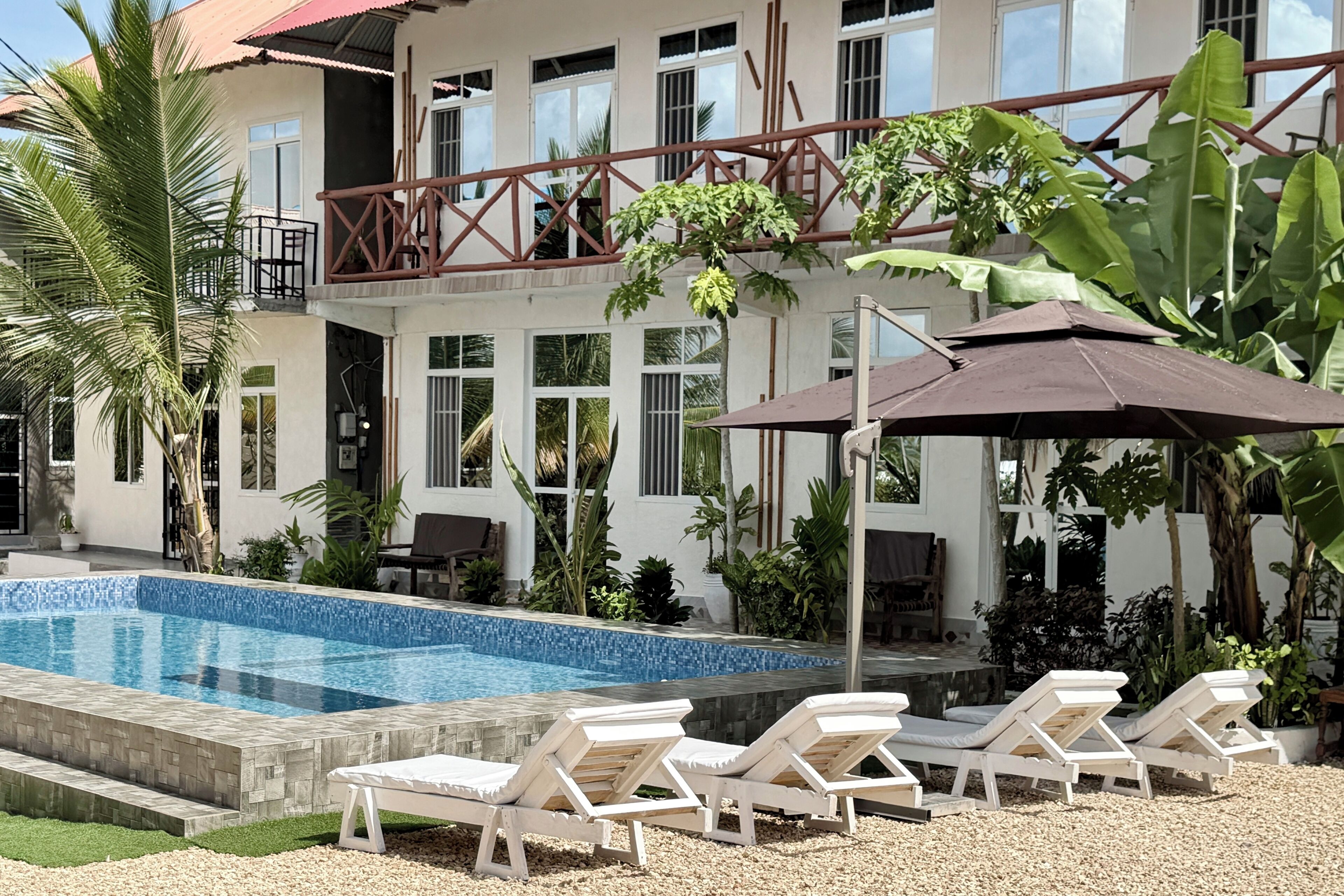 A pool area with lounge chairs and umbrellas, surrounded by a two-story building with large windows and balconies.