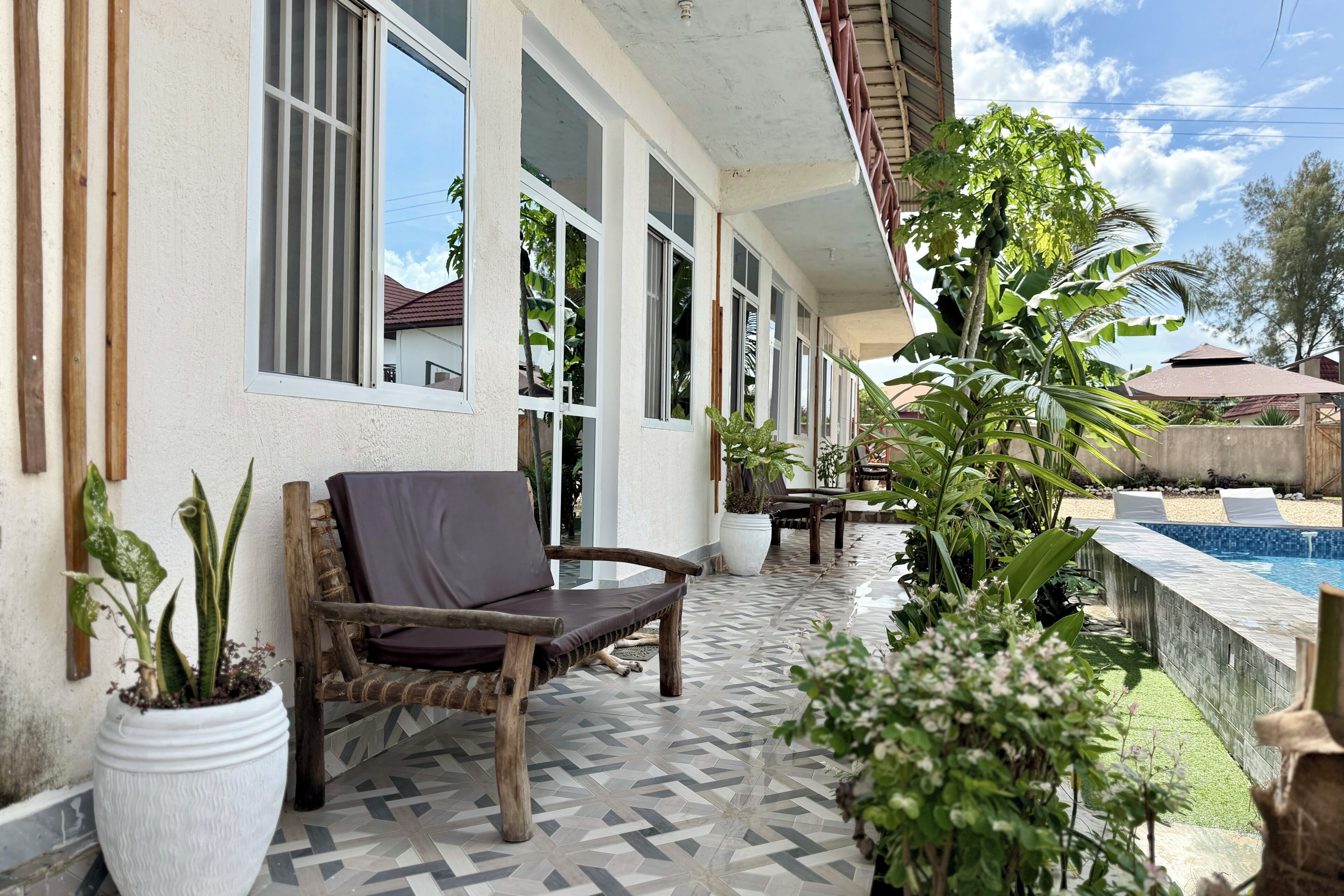 A covered outdoor area with a pool, potted plants, and a wooden bench.