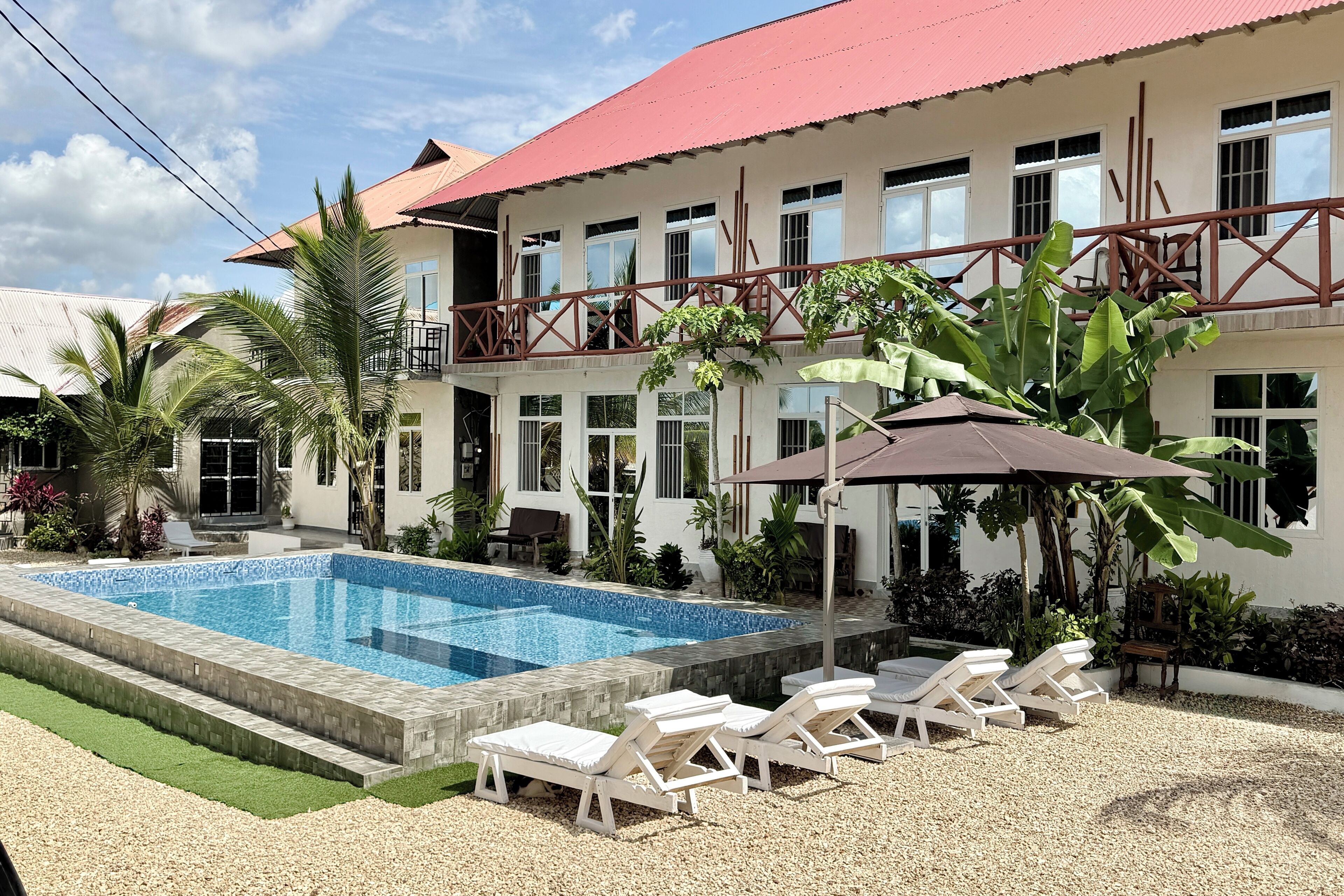 A two-story building with a swimming pool, outdoor seating, and a red roof.