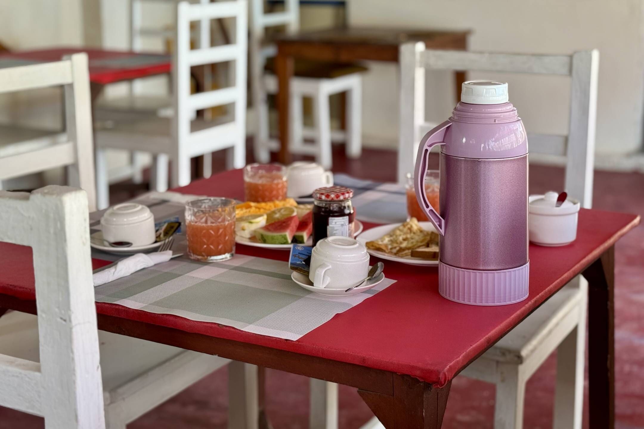 Una mesa de comedor con mantel rojo, sillas blancas y diferentes alimentos y bebidas.