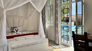 Ein Schlafzimmer mit Baldachinbett, Blick auf einen Swimmingpool und einer Essecke mit Tisch und Stühlen.