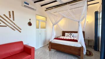 A bedroom with a wooden bed, white canopy, red sofa, and a small table.
