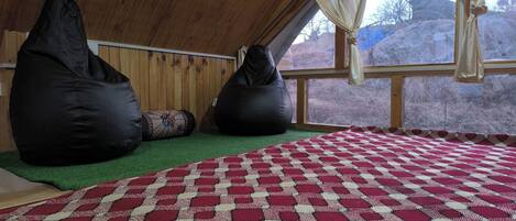Une pièce chaleureuse avec un plafond en pente, deux fauteuils en forme de poire, un tapis à motifs et une vue sur un paysage rocheux grâce à de grandes fenêtres.