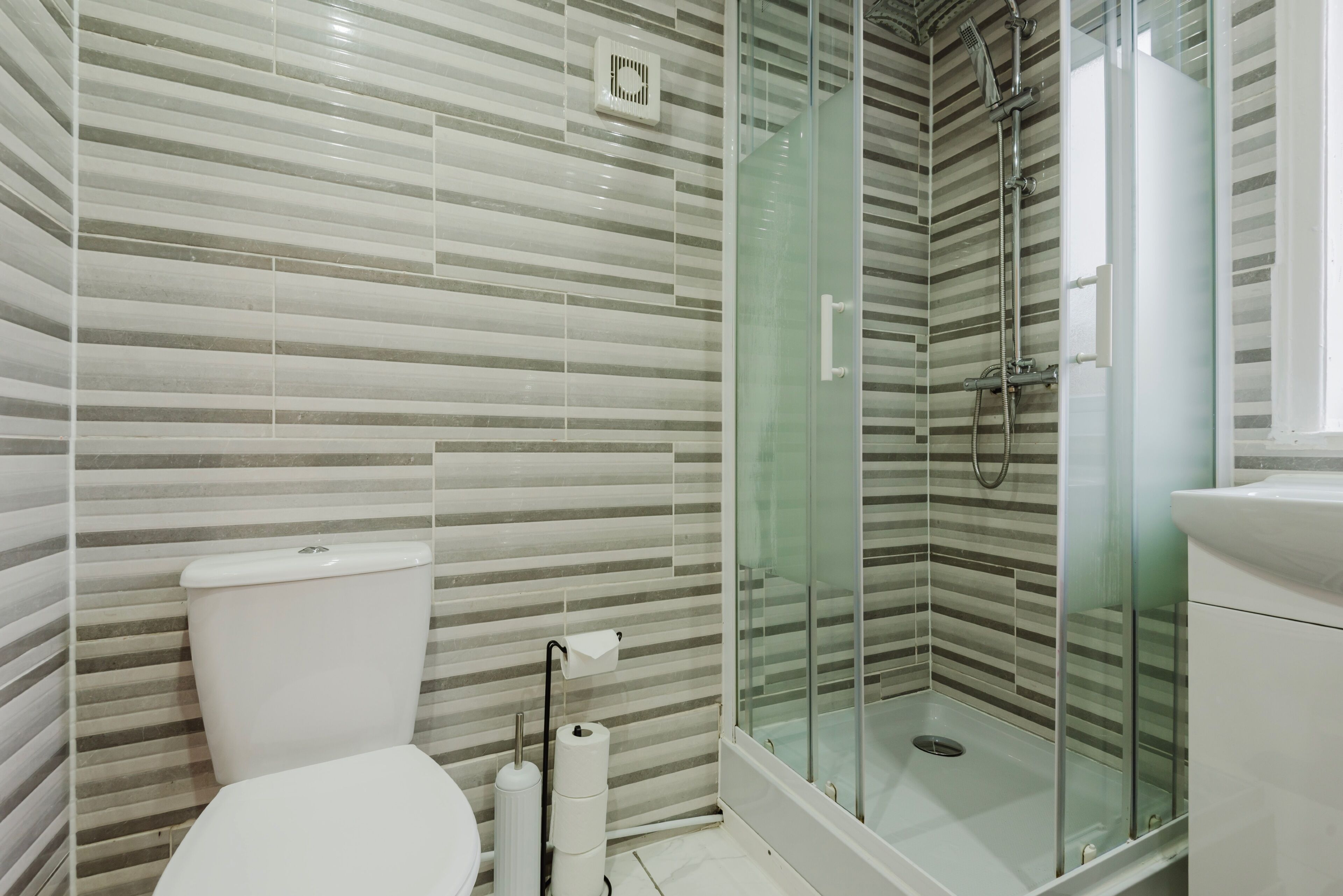 Ein modernes Badezimmer mit gestreiften Fliesenwänden, einer Duschkabine und einer weißen Toilette.