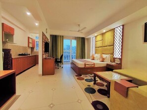 Ein modernes Hotelzimmer mit Bett, Sofa, Esstisch, Küchenzeile und einem Balkon mit Vorhängen.