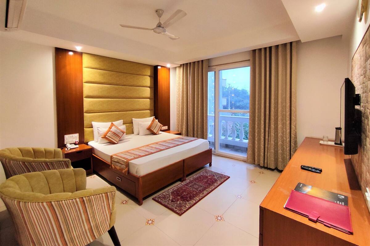 A hotel room with a bed, a desk, a chair, a ceiling fan, and a view of the outside.
