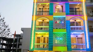 A multi-story hotel with balconies and a neon sign. - The Angel Hotel And Suites (Gurugram)