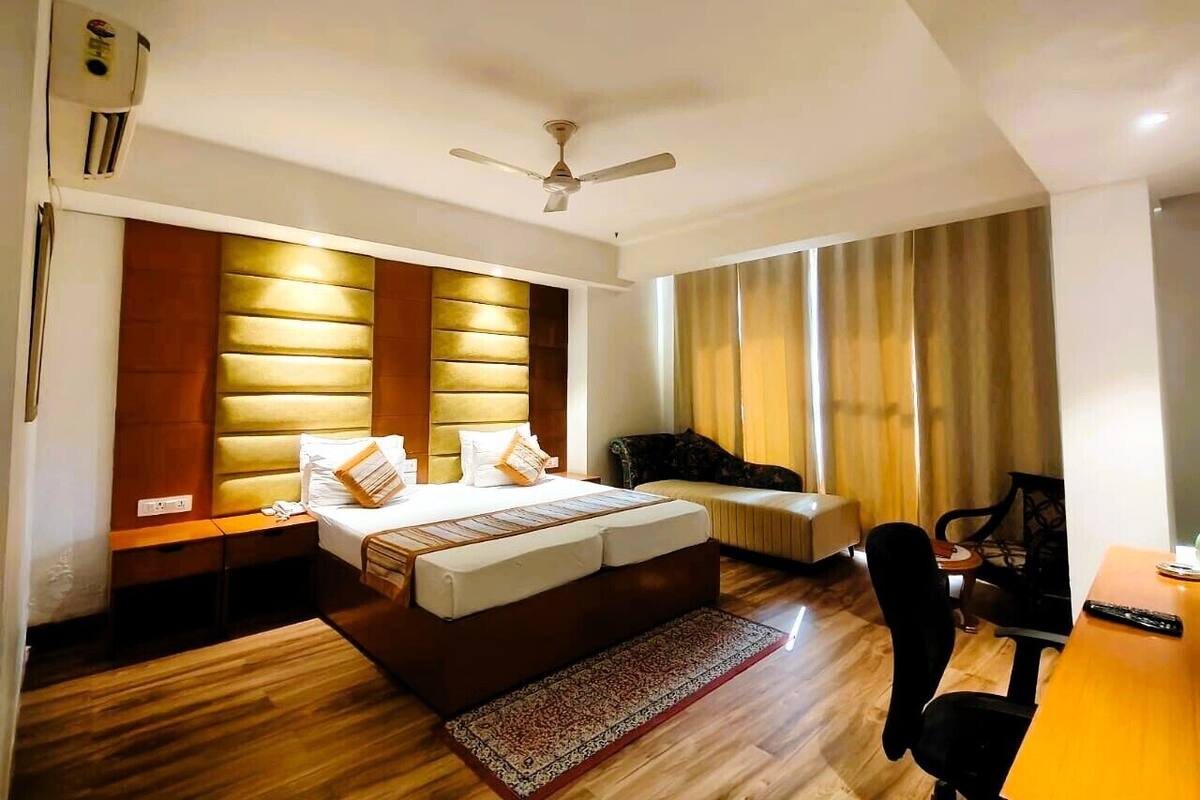 A hotel room with a bed, a desk, a chair, a ceiling fan, and a window with curtains.