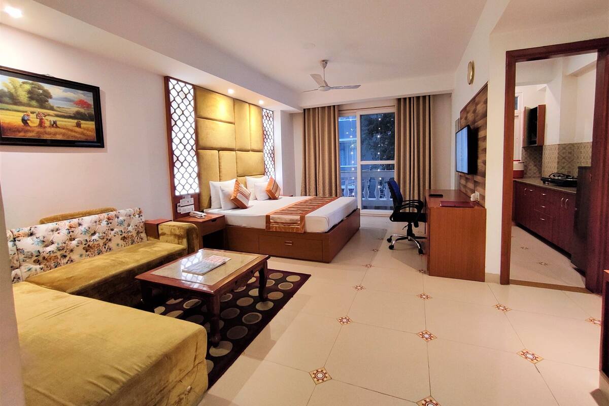 A hotel room with a bed, a sofa, a desk, a chair, a TV, and a window with curtains.