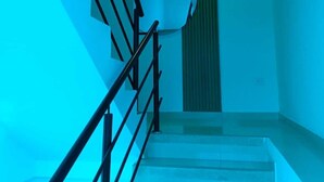 Una escalera con barandas negras que lleva a un rellano con una puerta verde y un objeto circular blanco en la pared.