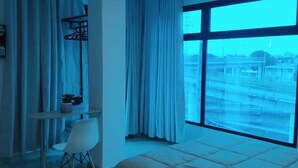 Un dormitorio con una cama grande, un escritorio con silla y vistas a la ciudad a través de amplios ventanales.