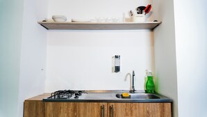 Una cocina con un armario de madera, una estufa a gas, un lavamanos y un estante con una taza de café y utensilios.