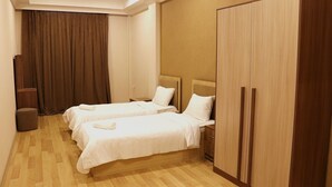 Een hotelkamer met twee bedden, een garderobe, een klein nachtkastje en een gordijn.