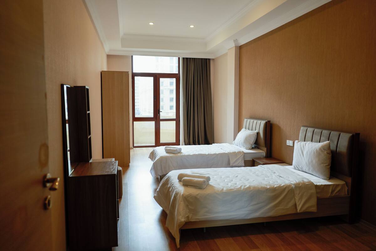 Une chambre d’hôtel avec deux lits, une télévision, une armoire et une grande fenêtre avec des rideaux.