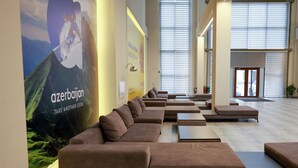 Een ruime lobby met een lange bank, een groot muurdecor en een lichte inrichting.