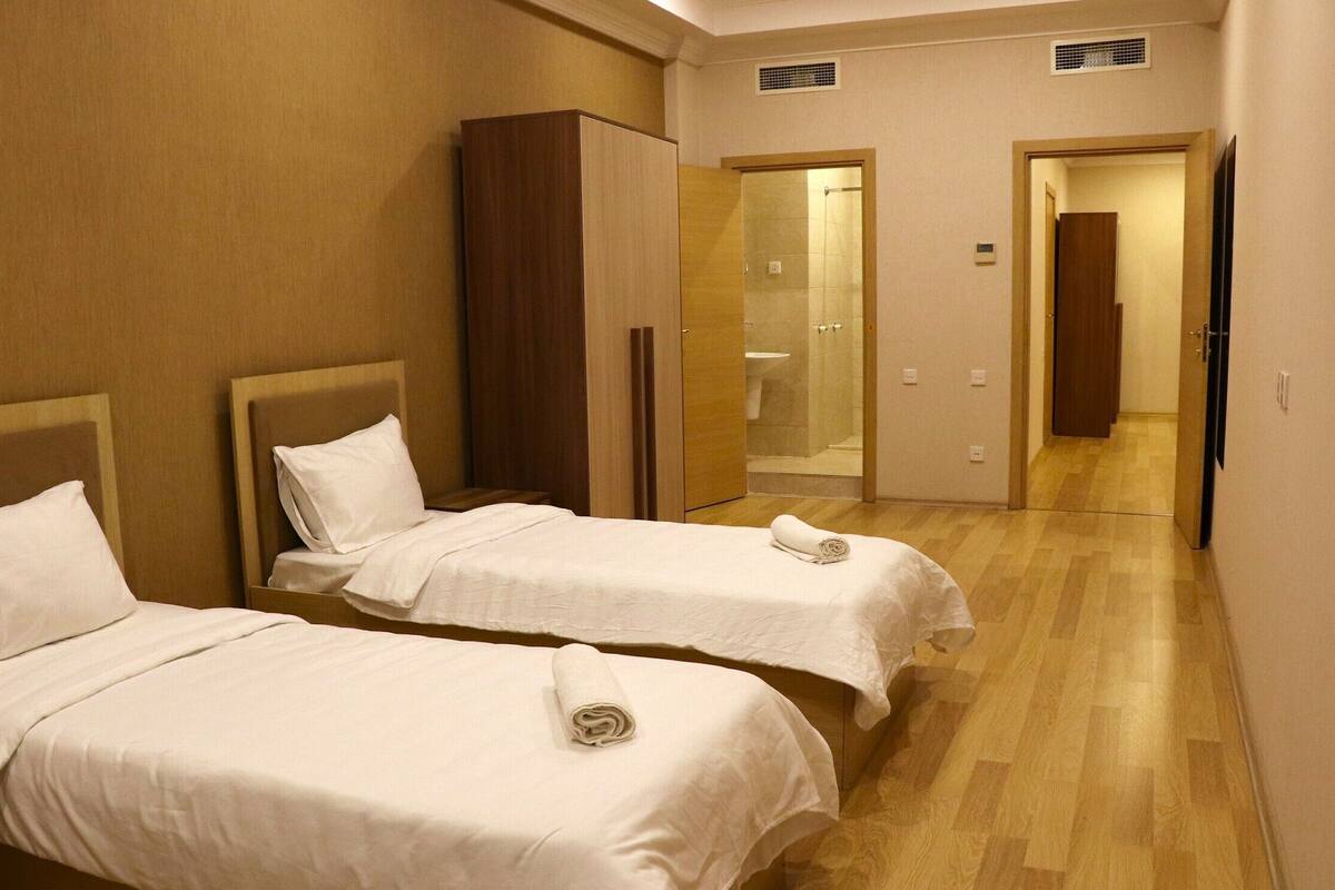 Une chambre d’hôtel avec deux lits, une armoire, un espace douche et un couloir menant à une autre pièce.