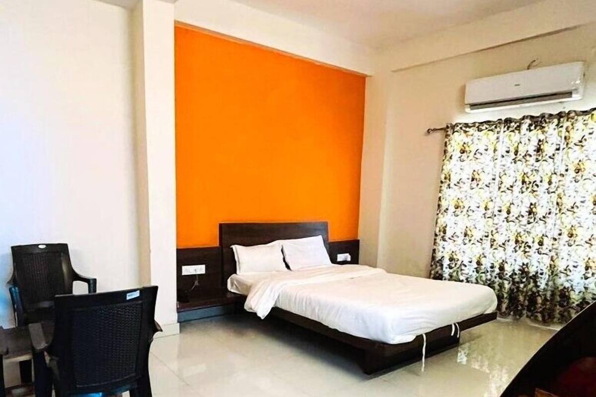 A hotel room with a bed, a desk with a chair, an air conditioning unit, and a window with curtains.