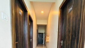 Un pasillo con puertas de madera, cada una identificada con un número. El suelo está cubierto de baldosas y hay una luz en el techo.