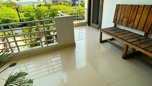 Un balcone con una panca in legno, una pianta in vaso e vista su edifici e vegetazione.