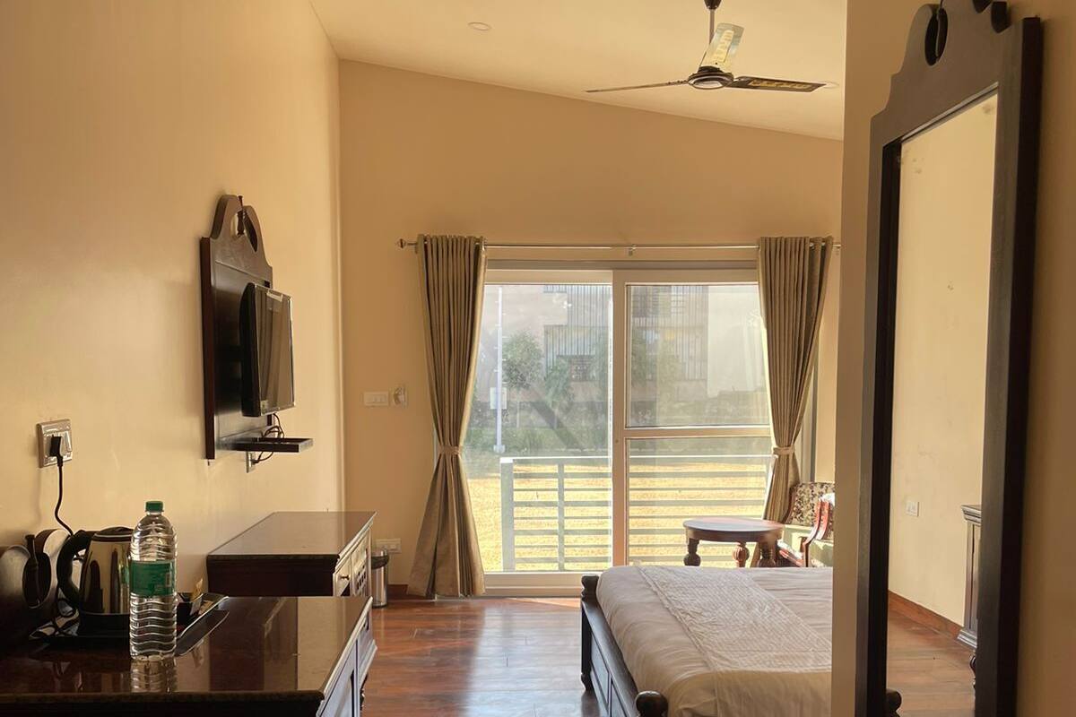 Habitación de hotel con cama, escritorio con silla, televisor montado en la pared, espejo grande y puerta corrediza de vidrio que da a un espacio exterior.