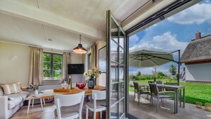 Ein modernes Wohnzimmer mit einer Couch, einem Esstisch und Stühlen, einem Fernseher und einer Schiebetür zu einer Außenpatio mit Tisch und Stühlen.
