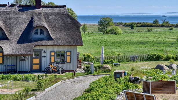 Ein Haus mit einem Strohdach, Blick auf das Meer, einem Fahrrad und einer Holzbank.