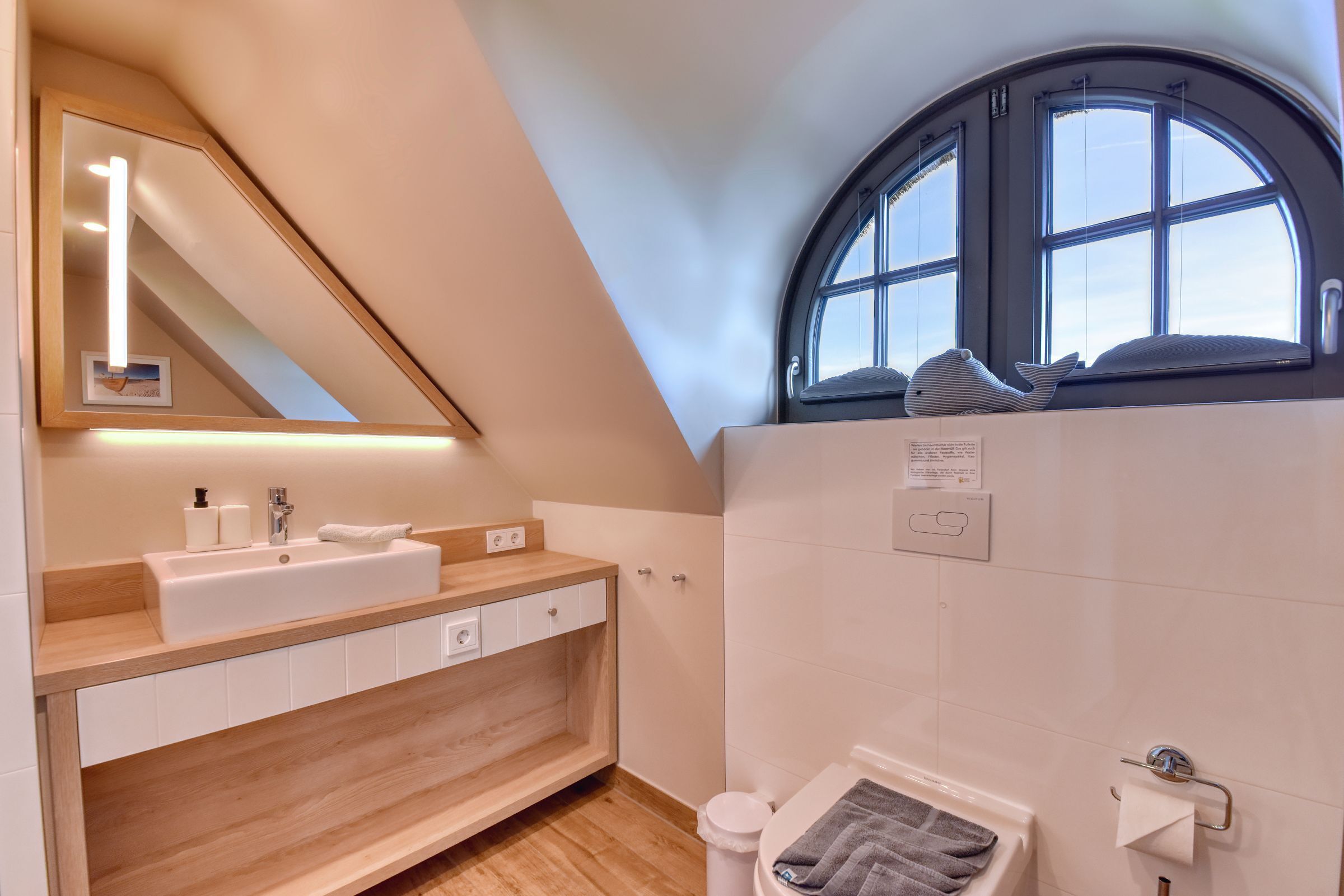 Un baño moderno con tocador de madera, un espejo grande, una ventana con vistas y un inodoro.