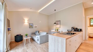 A modern kitchen with a wooden countertop and cabinets, a dining area with a white table and chairs, a grey sofa, and a small black ottoman. - Newly built, modern, exclusive - that describes the Klein Stresow vacation village (Klein Stresow)